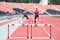 Two female sportswomen are jumping over an obstacle. Running with hurdles. Active lifestyle.