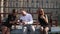 Two female students and a male student sit on a bench in sunny weather using smartphones