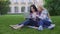 Two female students sitting on grass and choosing new dresses on laptop, device