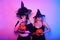 Two female witches in hats are holding pumpkins in their hands. Woman celebrating Halloween, photo in neon light