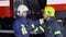 Two firefighters in protective clothing in helmets with fire engine, friendly handshake