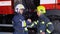 Two firefighters in protective clothing in helmets with fire engine, friendly handshake