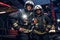 Two firemen hug and looking at the camera standing near the fire truck at night in a fire depot