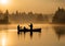 Two fishermen fishing in a misty and sunny lake.