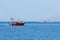 Two fishing boats in the open sea, surrounded by gulls, blue water, sunny day.