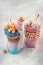 Two freak shakes topping with pink and blue donuts over grey background