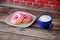 Two fresh donuts in pink and white glaze on a plate and a blue cup of cappuccino on a wooden table