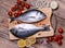 Two fresh gilt-head bream fish on cutting board with lemon, onion and tomato