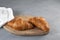 Two fresh golden croissants lie on a wooden serving board. Gray background, copy space