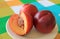 Two Fresh Ripe Nectarine Whole Fruits with One Cut Nectarine on a White Plate Served on Vibrant Color Tablecloth