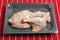 Two fresh uncooked duck legs on a grey plastic trey vacuumed packed for freshness, on a red butcher apron. Poultry product. Meat