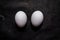 Two fresh white eggs lying down on black surface