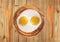 Two fried eggs on wooden plate, knife and fork on wooden table