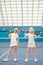 Two friendly girls in white sportswear standing on tennis field at stadium