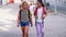 Two friendly preteen girls with backpacks talking while walking along city street on sunny summer day