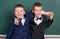 Two friends, elementary school boy near blank chalkboard background, dressed in classic black suit, group pupil, education concept