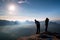 Two friends. Hiker thinking and photo enthusiast takes photos stay on cliff. Dreamy fogy landscape, blue misty sunrise in a beaut