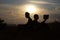 Two friends sitting on the hill of reading a book and sitting on a laptop on the background of a beautiful sunset