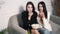 Two friends stylish brunette women are sitting on a sofa and eating popcorn