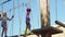 two frightened but brave girls in helmet, T-shirt and shorts climbs in rope park