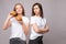 Two frowning young beautiful woman holding appetizing harmful burger looking at camera