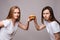 Two frowning young beautiful woman holding appetizing harmful burger looking at camera