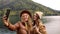 Two funny attractive girls young women fashionably dressed on vacation on a lake in the mountains take a selfie on the