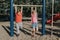 Two funny Caucasian friends hanging on pull-up bars in park on playground. Summer outdoors activity for kids. Active children boy