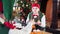 Two funny elves sitting at table on Christmas background. Girl elf tries to take sweets and another elf interferes her.