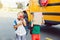 Two funny happy Caucasian boys students kids standing near yellow bus on 1 September day