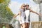 Two Funny and Laughing Teenage Girlfriends Embracing Together. Posing Against Fountain in Park Outdoors