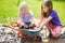 Two funny little girls playing in a large wet mud puddle on sunny summer day. Children getting dirty while digging in muddy soil.