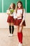 Two funny schoolgirls in school uniform are standing with books on the background of the school board