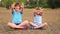 Two funny sisters sitting on grass with crossed legs and waving painted hands in summer