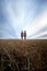 Two ghostly looking, scary, young women in striped dresses standing in front of dramatic skies on a stubble field, wide angle,