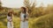 Two girl teenagers in white dresses and straw hats with flowers bouquet posing on nature background at sunny summer day