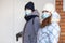 Two girlfriends coming indoor in face mask, holding handle of the door. Winter season, warm clothes