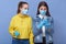 Two girlfriends in medical masks and gloves read breaking news and using mobile phone, being shocked, wearing casual attire,