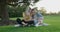 Two girlfriends sitting on green grass of lawn smiling talking looking together at smartphone screen