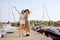 Two girls on the background of yachts, sailing boats are smiling, looking at the camera. Brunette in a hat and blonde in a dress