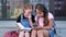 Two girls with backpack sit and read book with phone