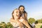 Two girls best friends having fun outdoor in a green nature park looking at camera laughing and joking. Young brunette woman