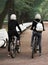 Two girls on bicycles on a walk in a deserted park. Alley, benches, path sprinkled with gravel. Photo.