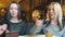 Two girls with blonde and dark hair are talking and eating desserts in a beautiful cozy restaurant during the daytime.