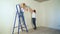 Two girls at construction site glues wallpaper to the wall