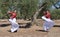 Two girls dance flamenco in an olive grove making a parallel movement