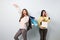 Two girls dressed in nice stylish clothes after shopping. One of them is happy holds lots of bags and another one sadly