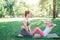 Two girls are excercising in park. Woman is sitting on her knees and holding her daughter`s feet while small girl is