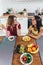 Two girls friends sitting in kitchen, eating fruits and vegetables.