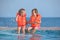 Two girls in lifejackets sitting on ledge pool